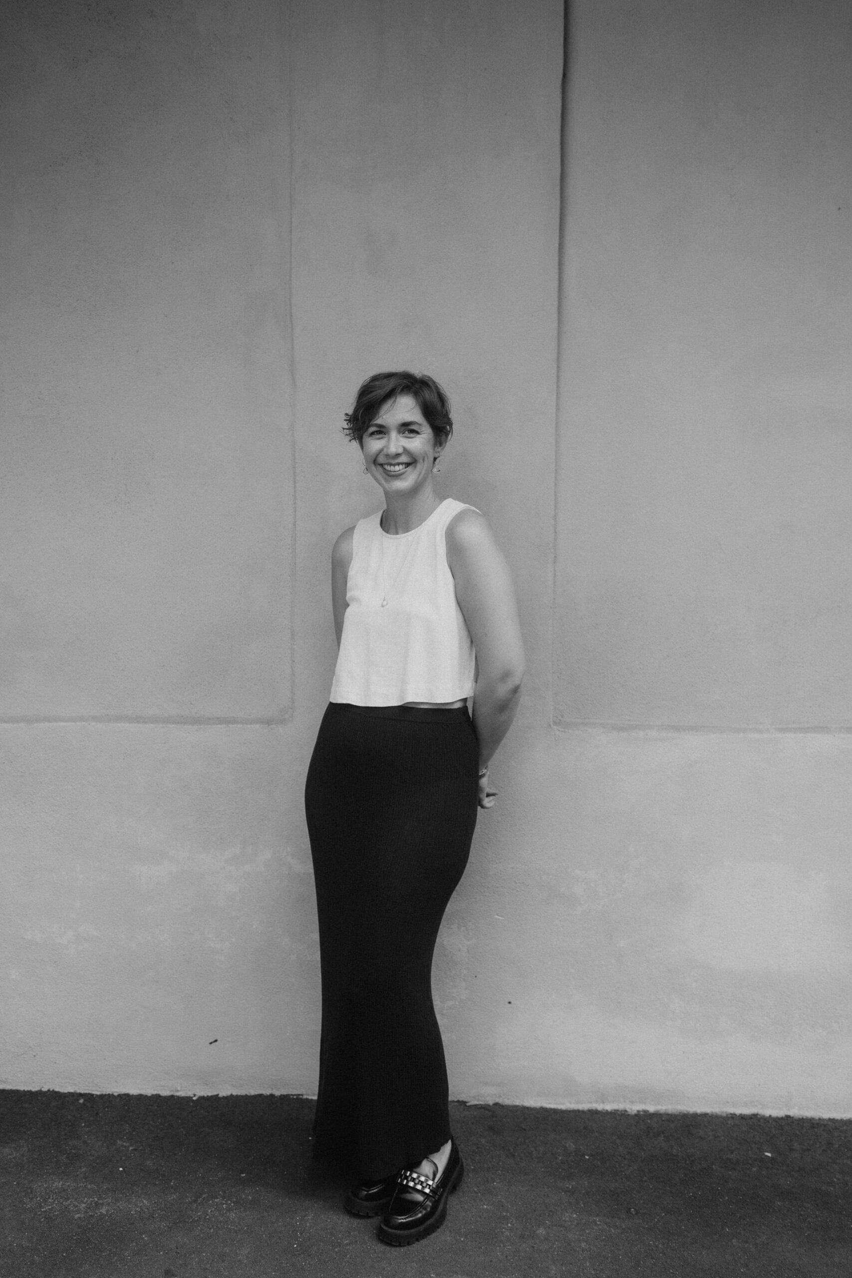 Fotografin_Jennifer Fotografin Jennifer steht vor einer Wand hat Hände hinter dem Rücken. Das Foto ist für ihre About-Seite.